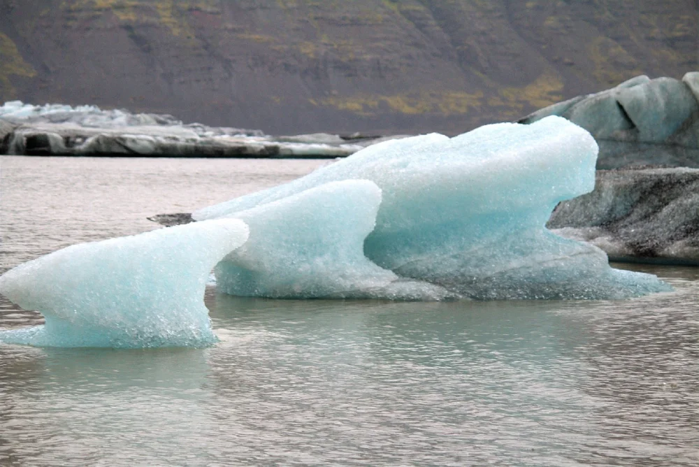 A striking iceberg floats in frigid waters, its sculpted surface hinting at ongoing melting—representing climate change impacts on polar environments.